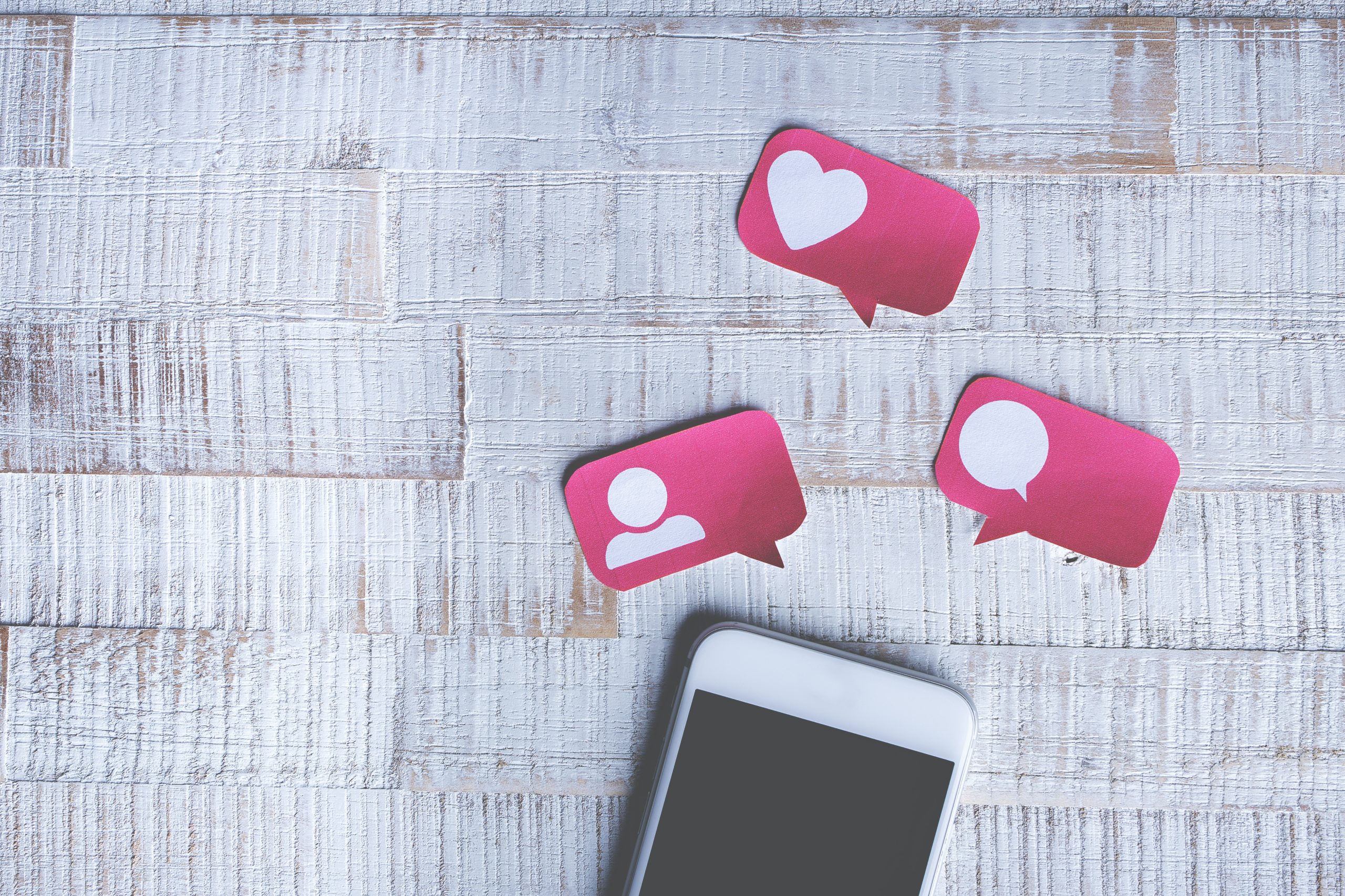 Phone on floor with paper cut out shapes around the phone. The paper has icons on them for a person, message speech bubble and a heart.